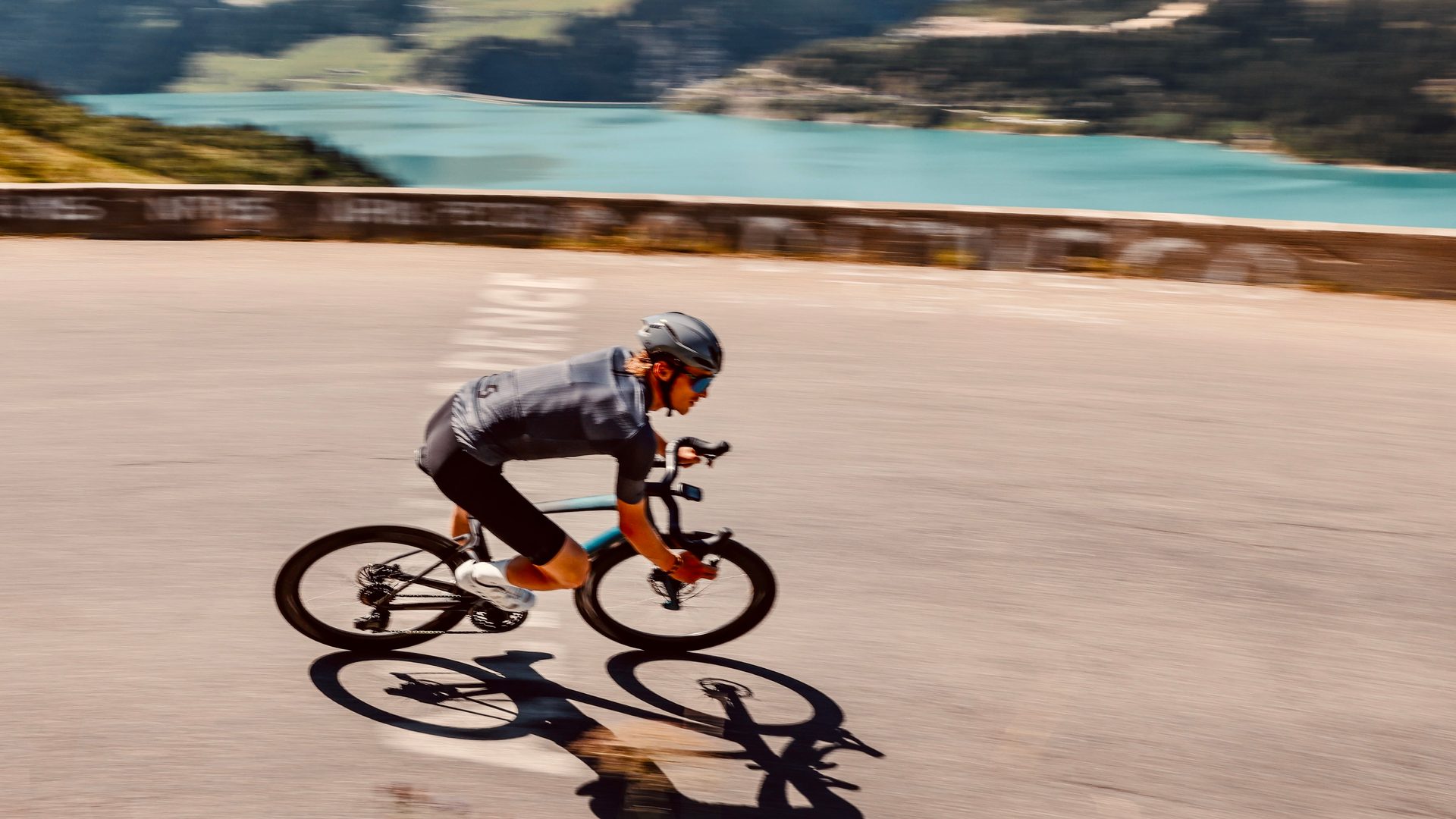 Cycliste sur une route de montagne, saisi en filé, au-dessus d'un lac de barrage
